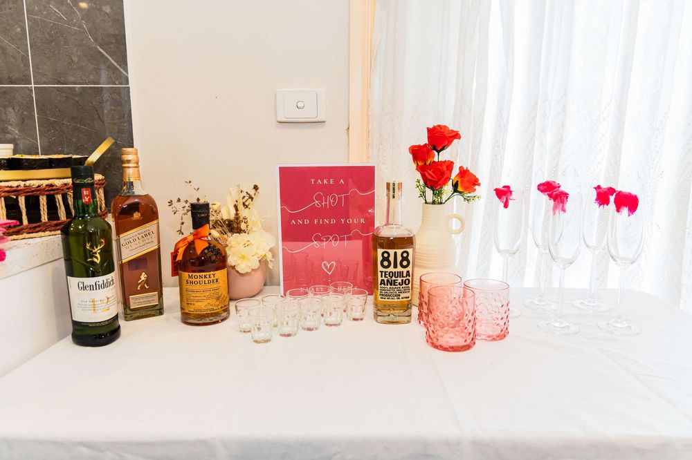 Pink and red Valentine's day party decorations with drinks and glassware on white table against window background.