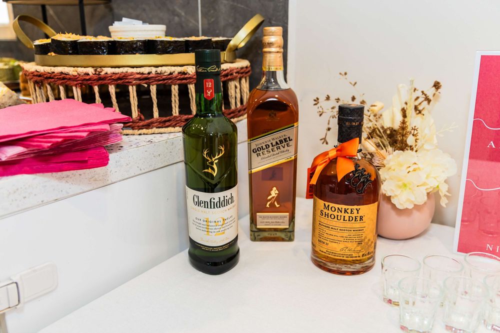 Various liquor bottles including Glenfiddich whiskey and wine sit on a white countertop with pink decor.
