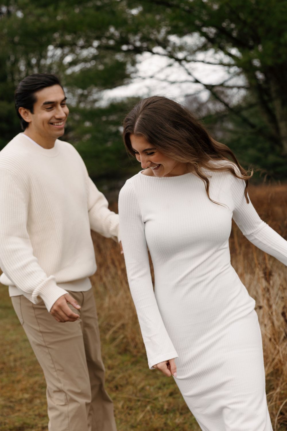 A couple in white and beige outfits share a tender moment outdoors during a photo session.
