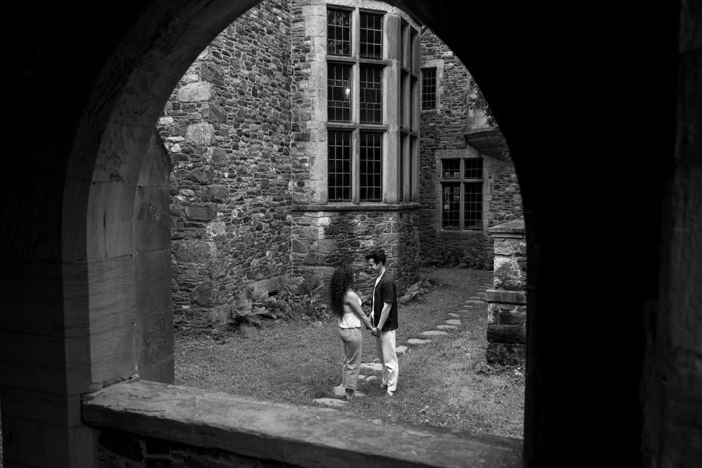 Black and white photo of a couple embracing in a historic stone courtyard, framed by an arched entrance.