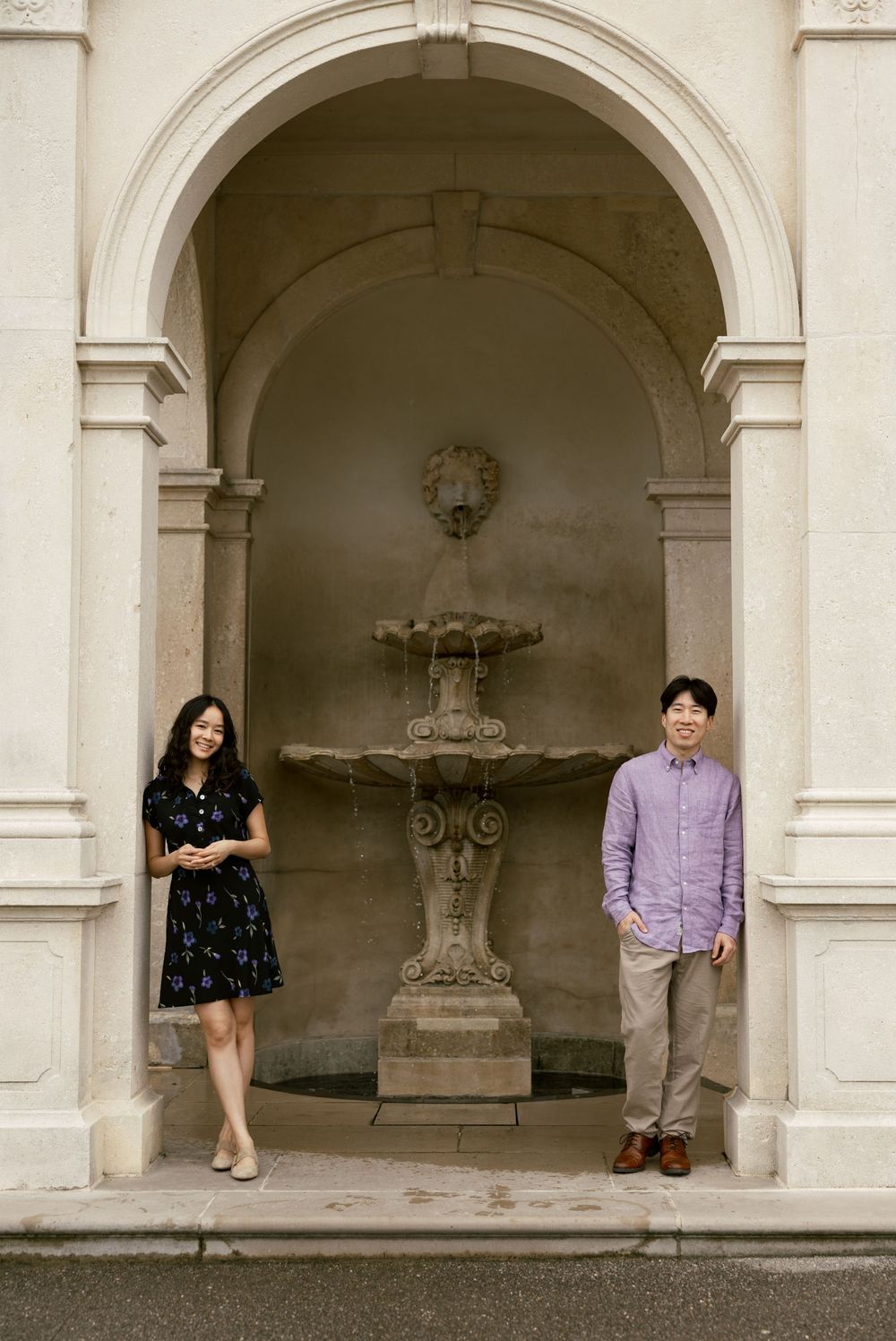 Two people pose playfully in arched stone alcoves of a classical building.