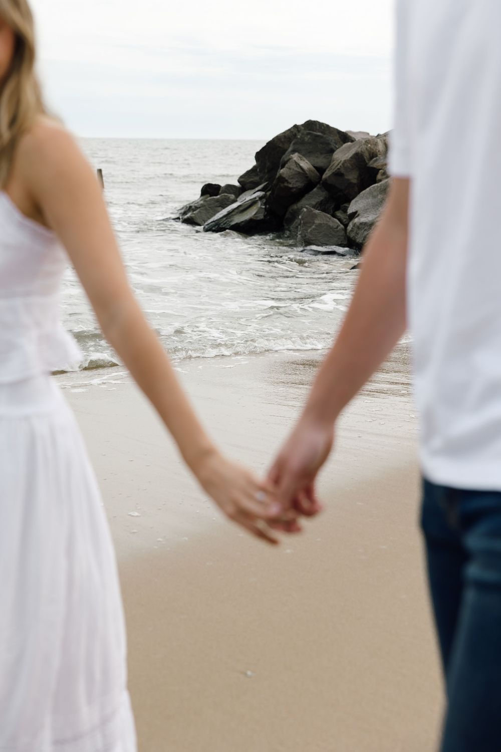 A couple holds hands tenderly while walking along the beach shore.