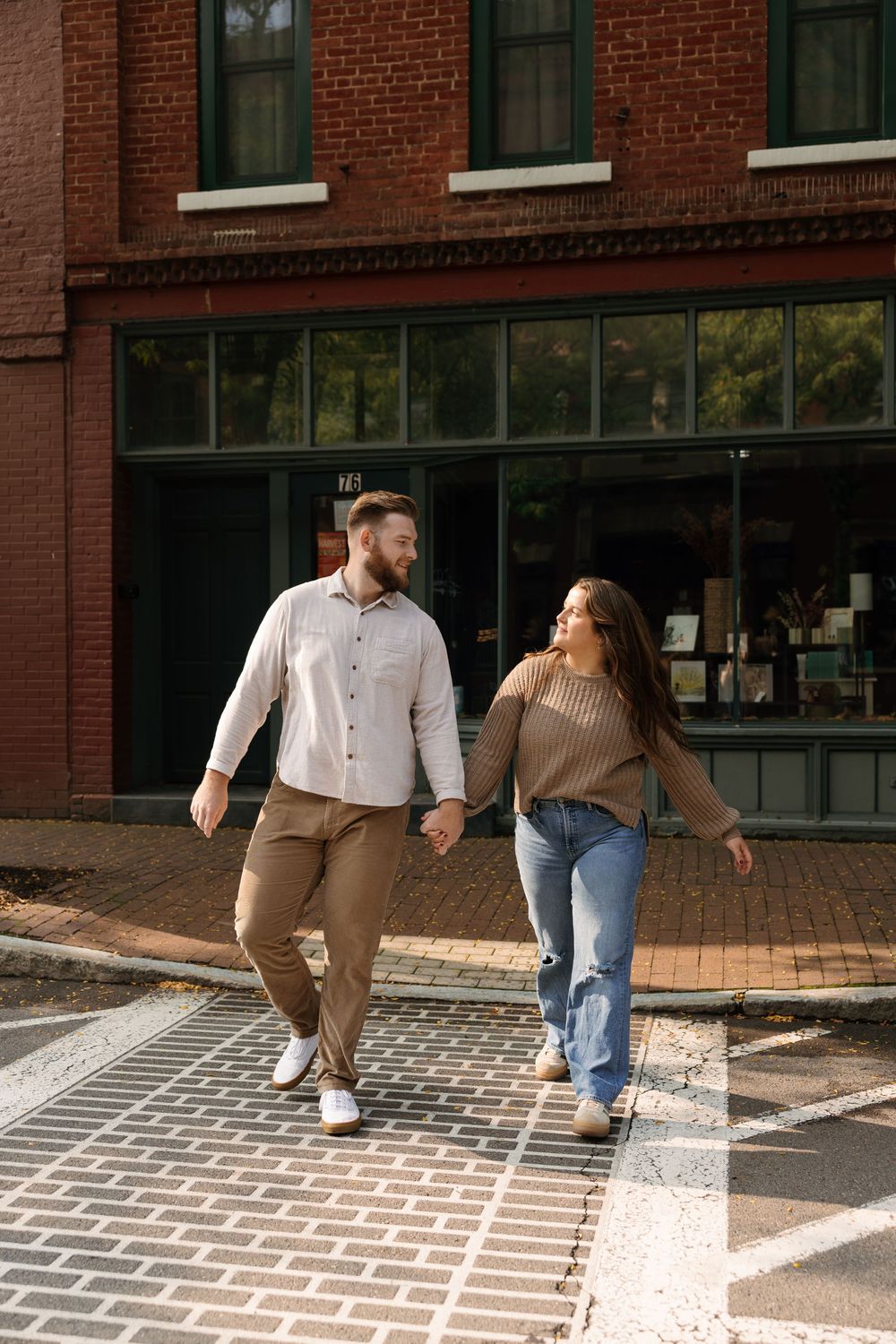 Casual engagement photo session on brick sidewalk showing playful walking poses.