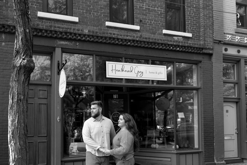 Urban engagement session with brick storefront backdrop in natural lighting.