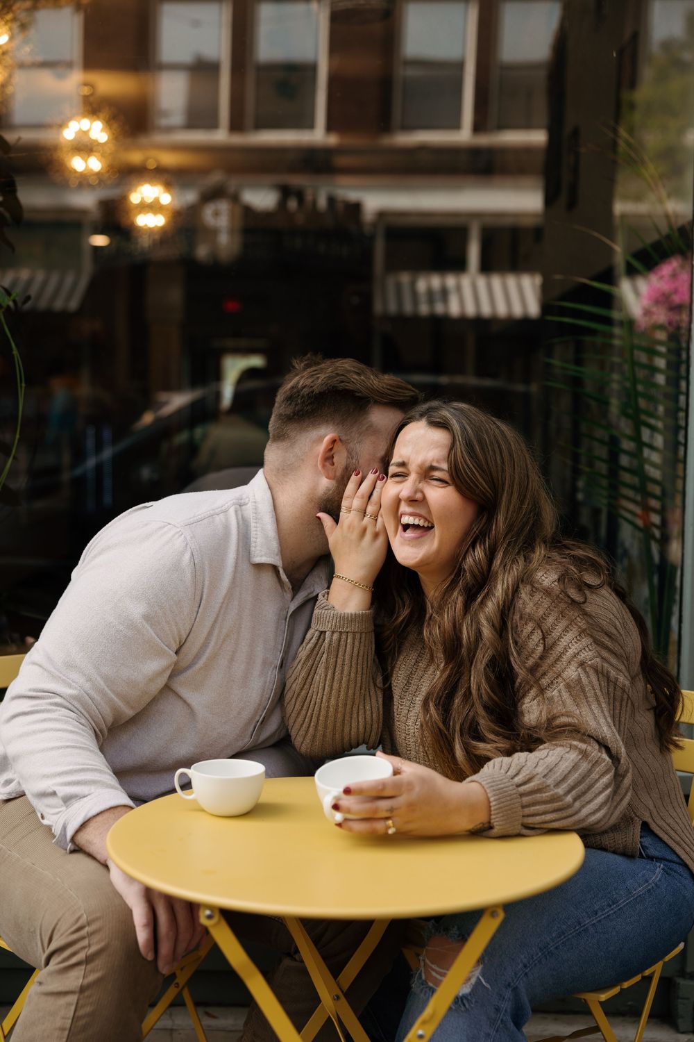Intimate engagement photos at outdoor cafe with yellow table and warm lighting.