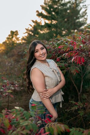 Autumn portrait session among vibrant red foliage and trees during golden hour sunset lighting.