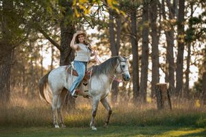 A couple shares a tender moment while standing next to a white horse in a sunlit forest setting.