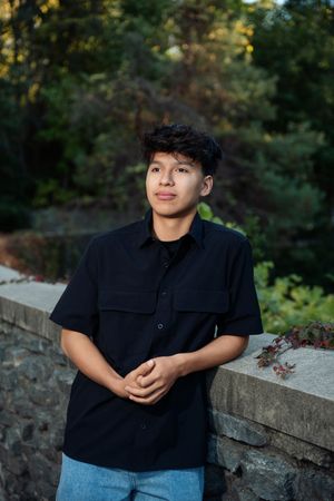 A series of outdoor portrait photos showing someone in a black shirt sitting on a stone wall with trees in the background.