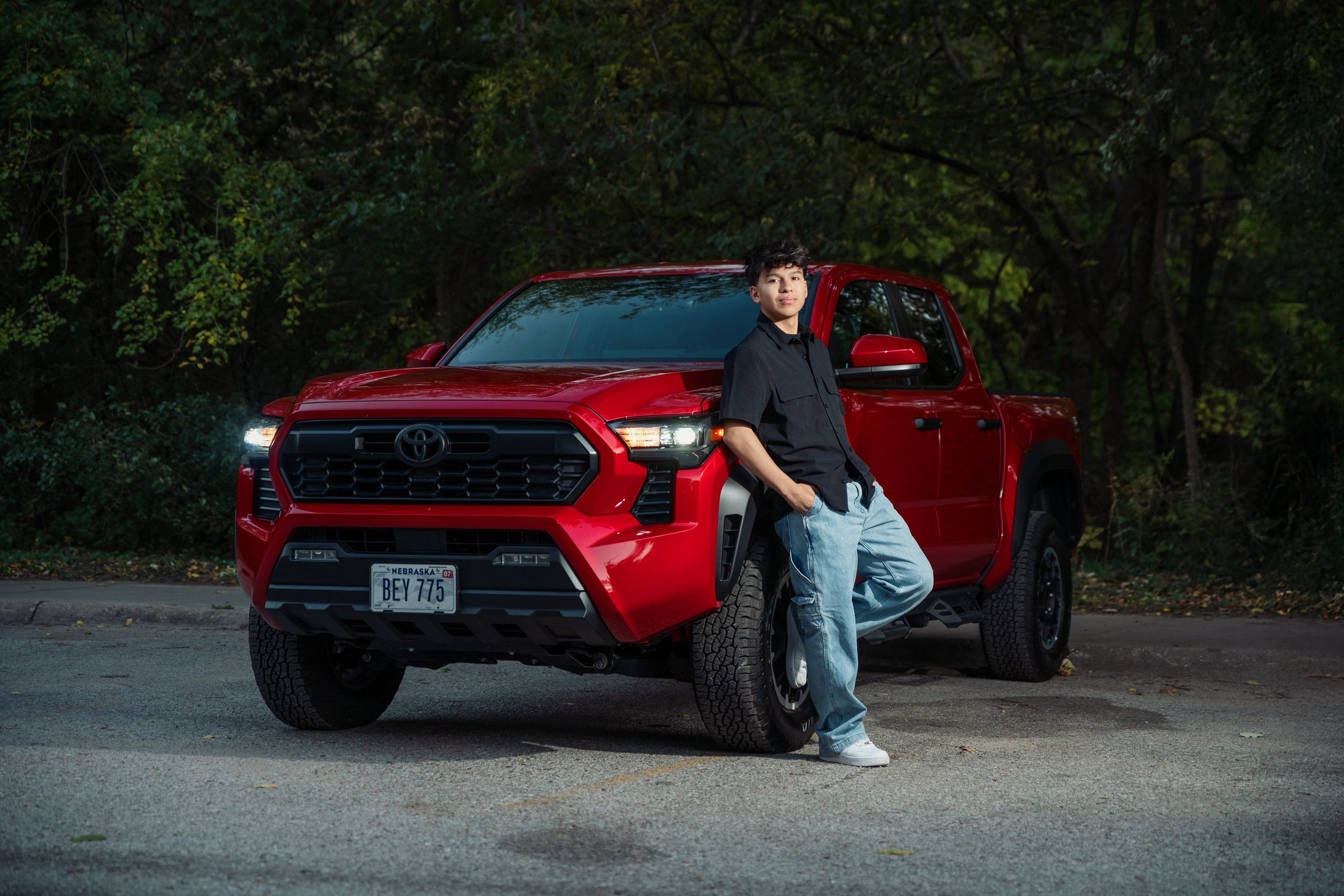 A red Toyota Tacoma truck parked on a dirt road in a wooded area during golden hour lighting.