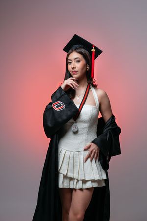 Artistic graduation portraits with white dress and black cap against pink backdrop.