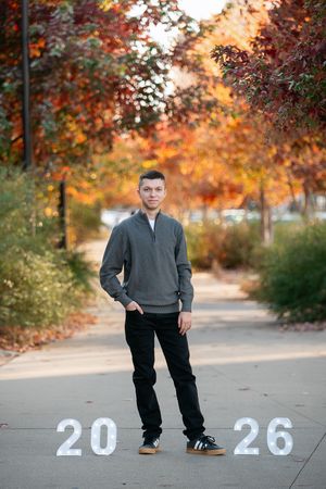 Senior portrait photo session outdoors with autumn trees showing vibrant orange fall colors in background.