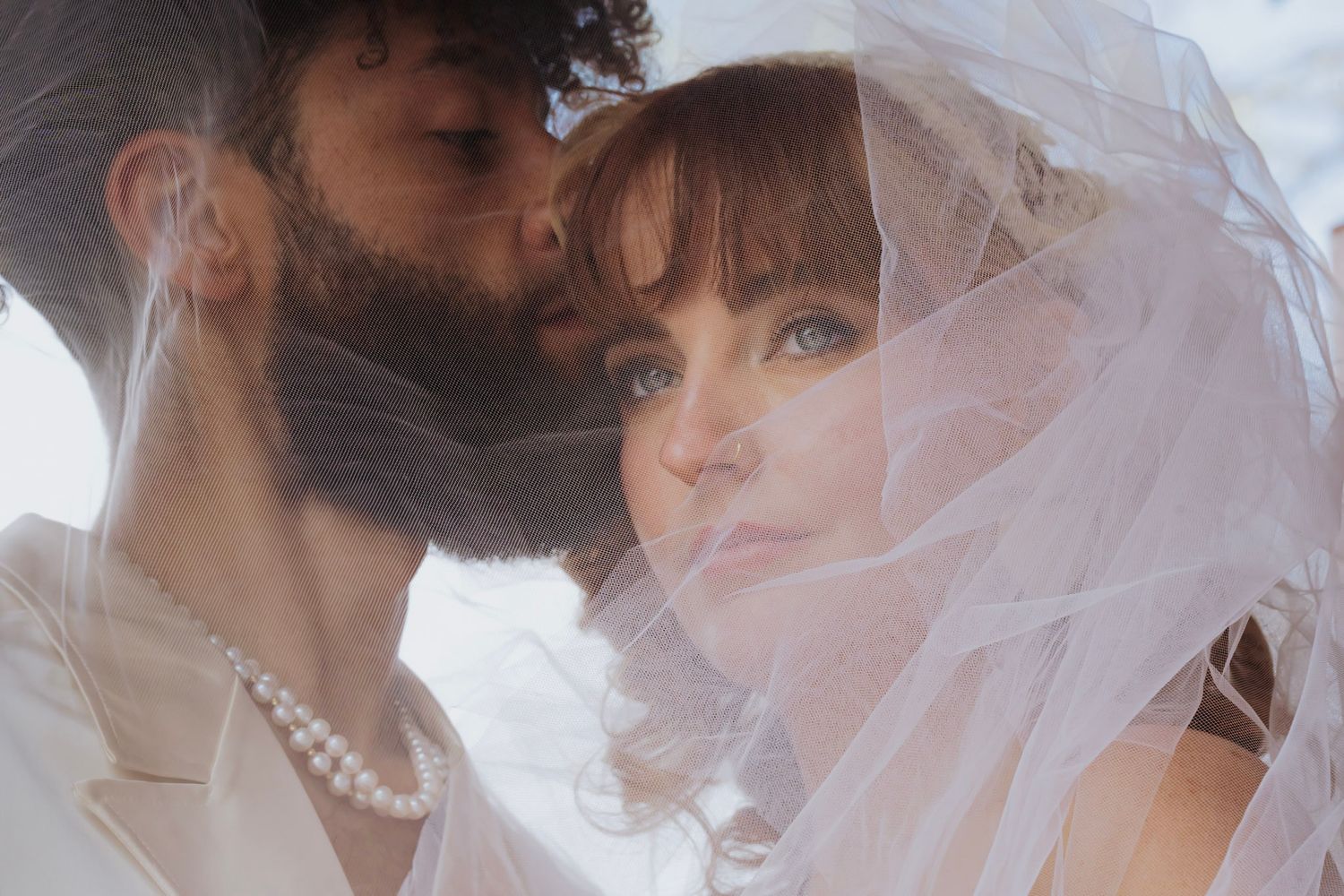 A romantic wedding portrait showing a couple embracing under a delicate white veil soft lighting. Intimate romantic elopement photographer