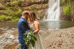 A couple shares an intimate moment in front of a majestic cascading waterfall on their wedding day.