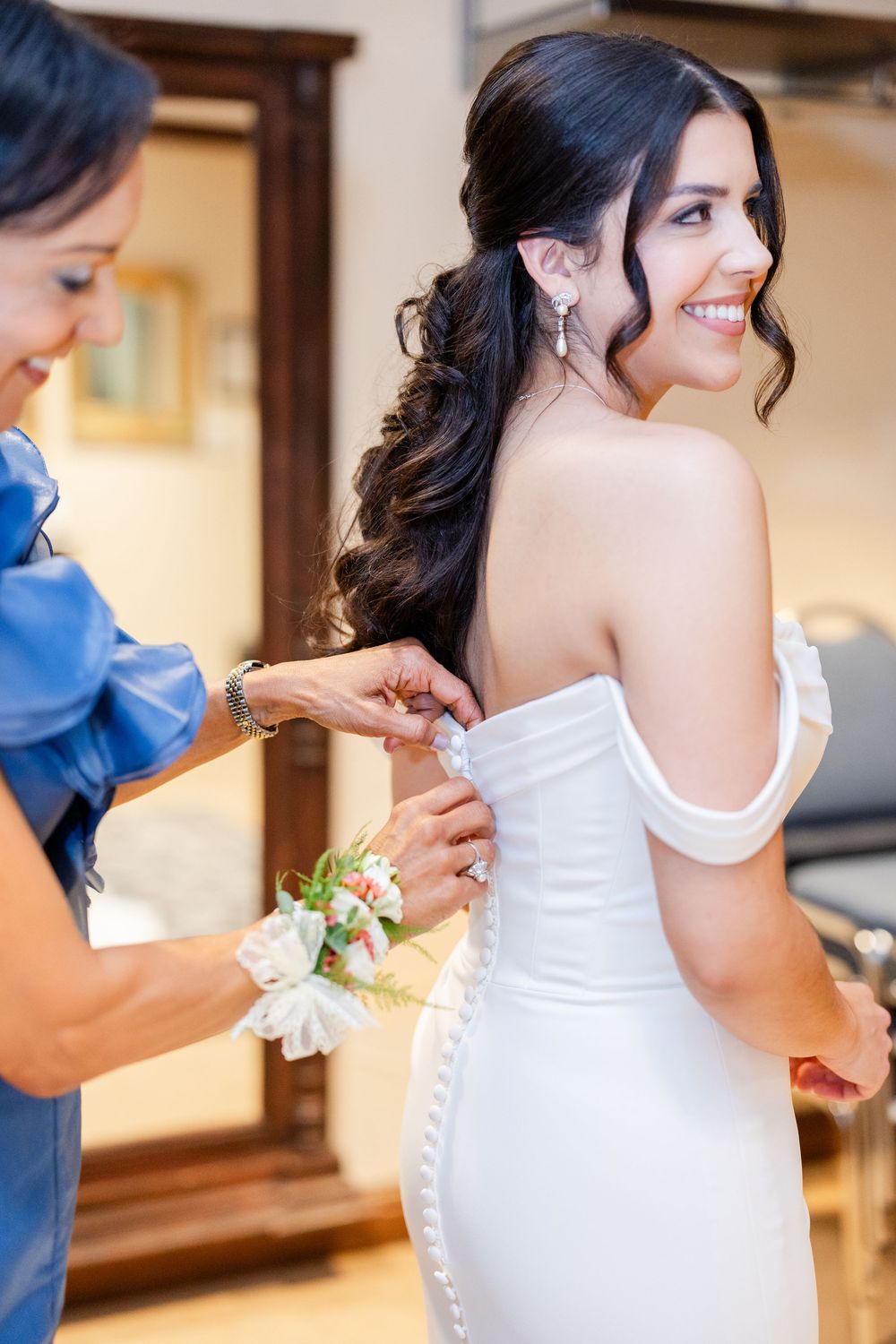 A bride in an elegant off-shoulder white dress smiles while getting ready for her wedding day.