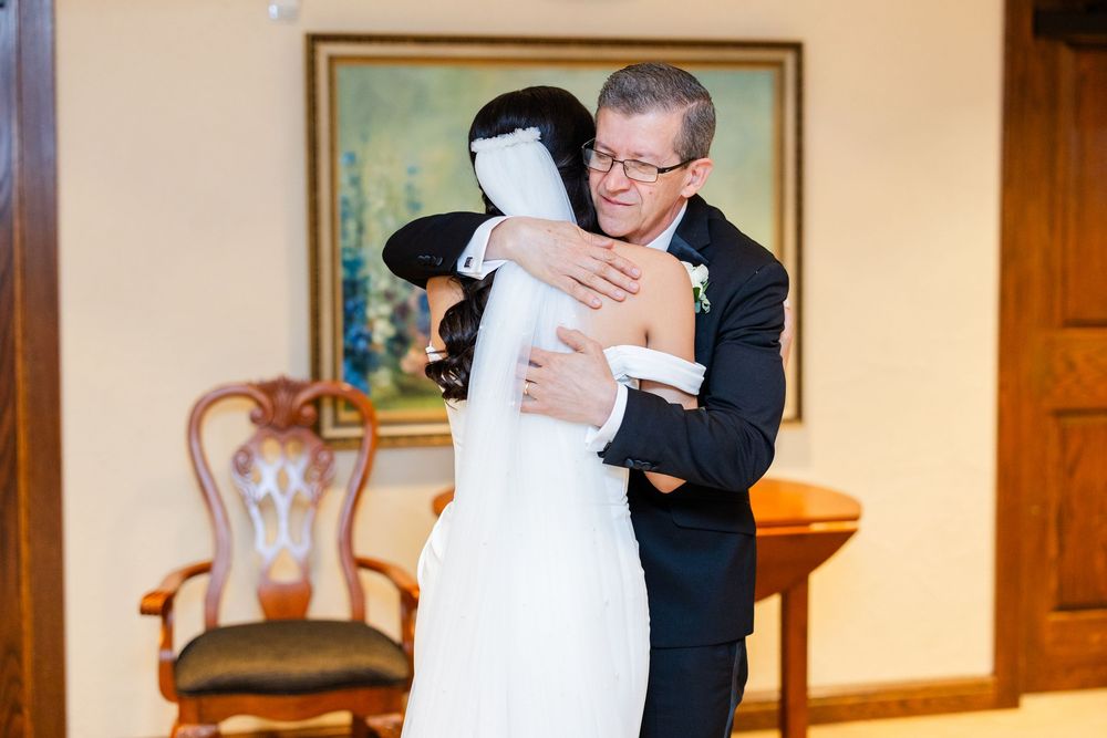 A tender wedding moment captured in an elegant room with framed artwork.