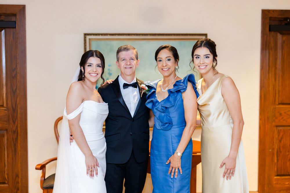 Wedding party group poses together in formal attire against interior wall with wooden doors.