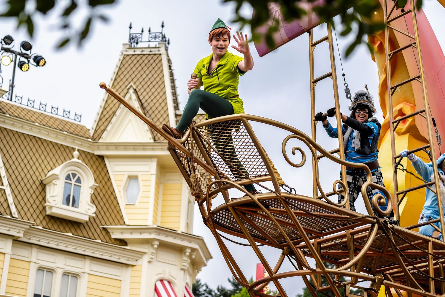 Performers in safety harnesses demonstrate acrobatic skills on a unique ship-themed structure in front of a vintage building.