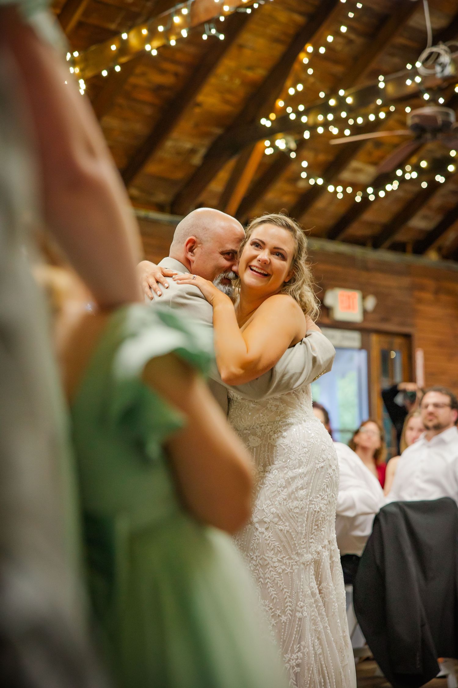 A couple shares a sweet moment while dancing in a rustic barn venue decorated with twinkling string lights.