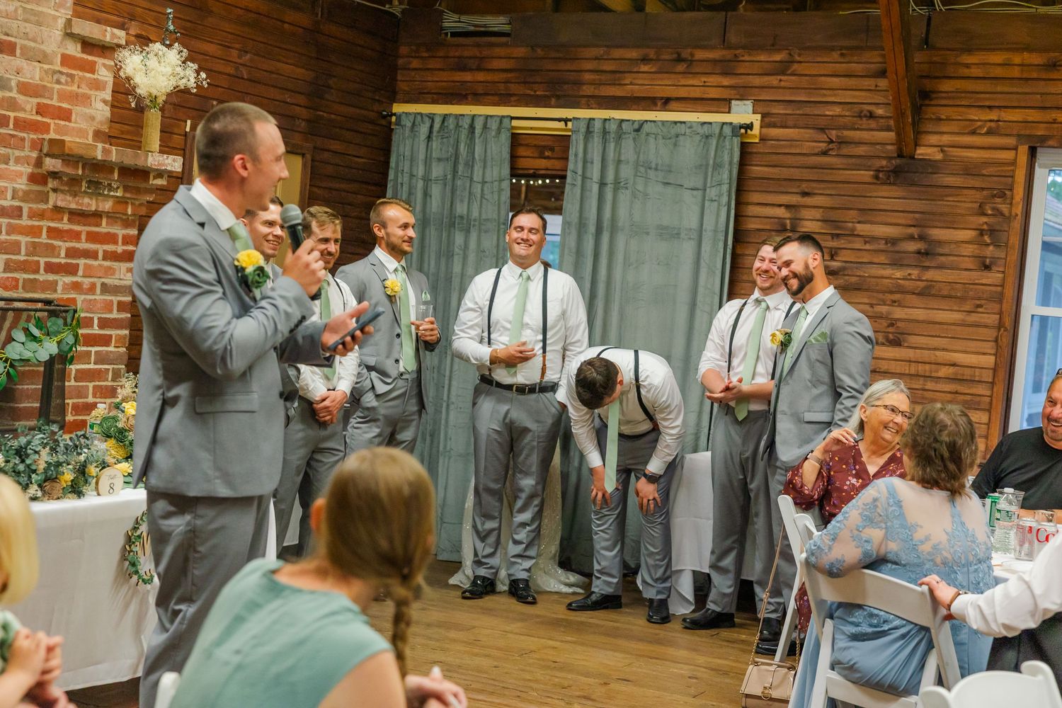 Groomsmen in light gray suits gather during a rustic barn wedding reception.