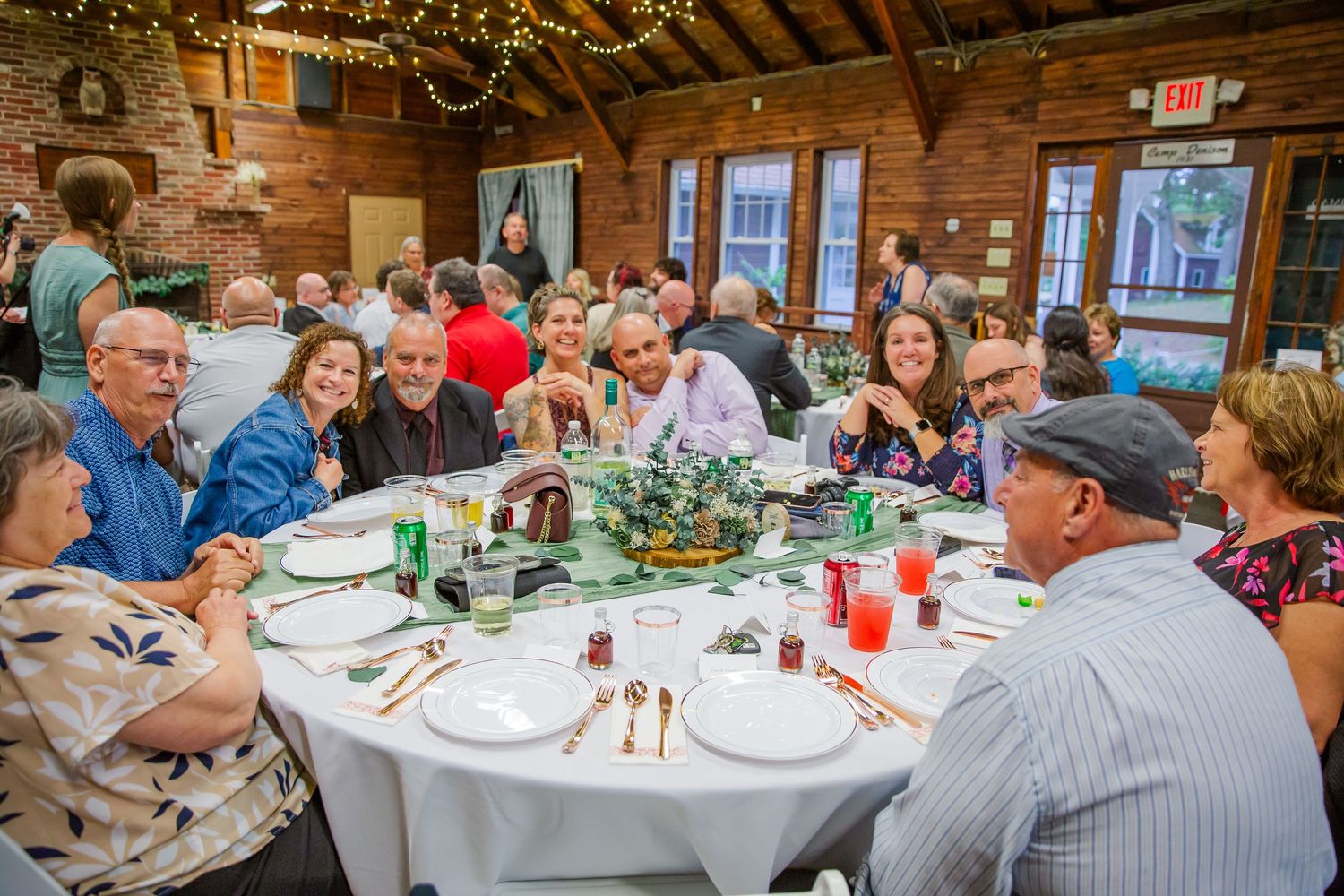 Party guests enjoy a festive meal at a round table in a rustic venue with exposed brick walls and hanging lights.