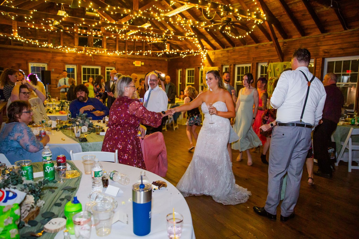 Reception guests dance and celebrate at a rustic barn wedding venue decorated with twinkling string lights overhead.