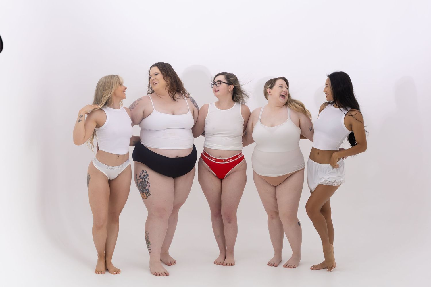 Group of diverse women in underwear standing together against white background showing body positivity.