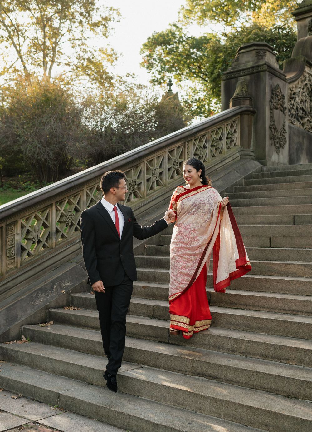 A couple in traditional wedding attire poses on stone steps during a sunset photo session at a park.