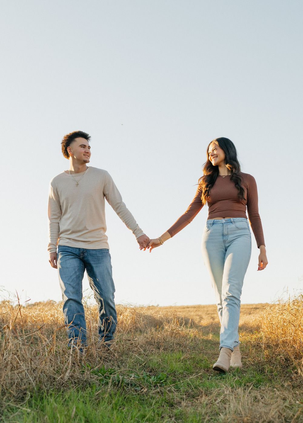A couple walks hand in hand through a golden field at sunset, creating a romantic silhouette against the warm sky.