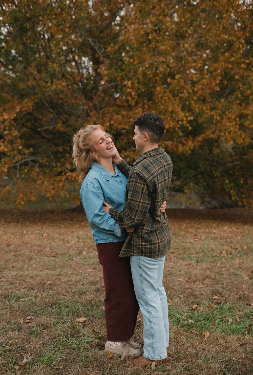 A couple shares a joyful moment together on an autumn day with golden leaves in the background.
