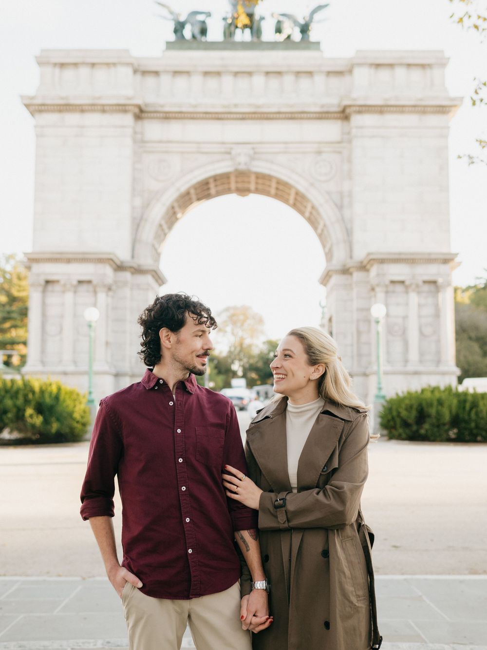 A couple shares joyful moments together in front of a grand stone archway on a sunny afternoon.