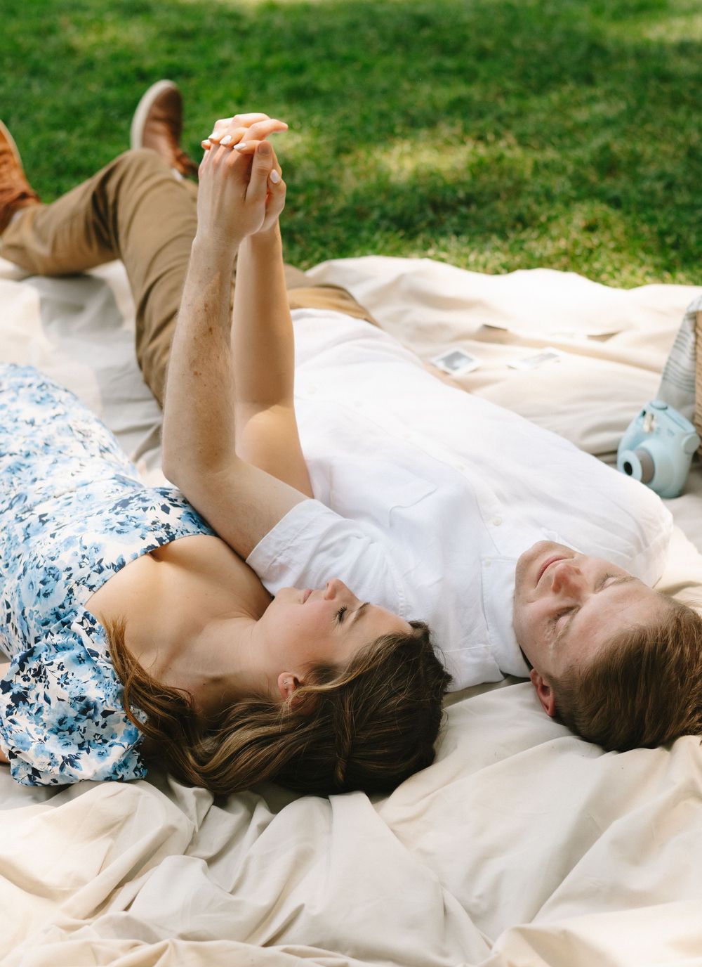 A person in a white dress lying on a blanket outdoors in the grass on a sunny day.