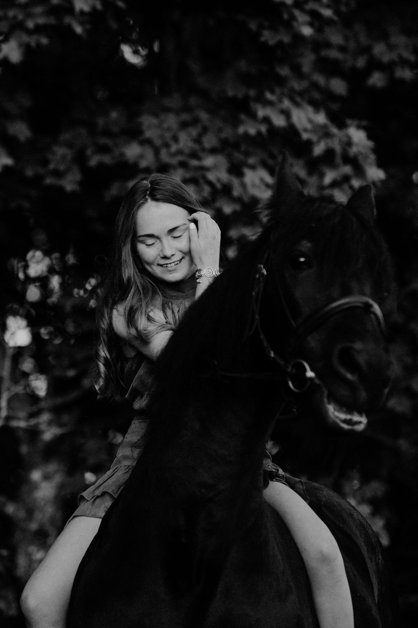 Black and white photo of a rider enjoying a moment with their dark horse in a natural outdoor setting.