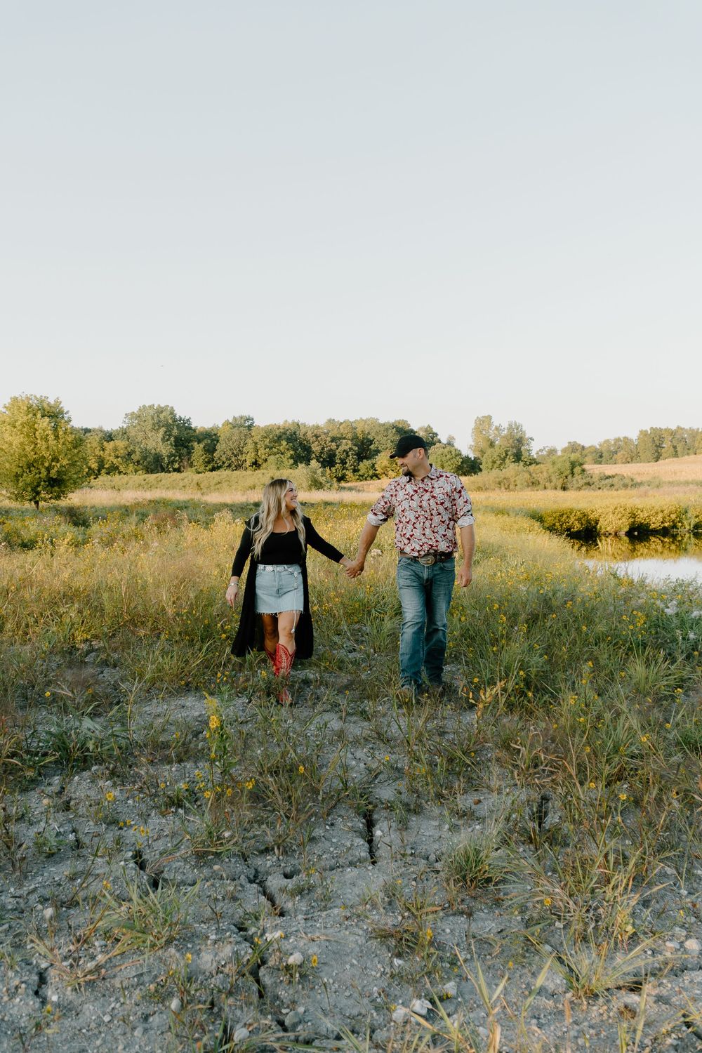 People walking together through a sunny meadow with tall grass and scattered vegetation on a late summer afternoon.