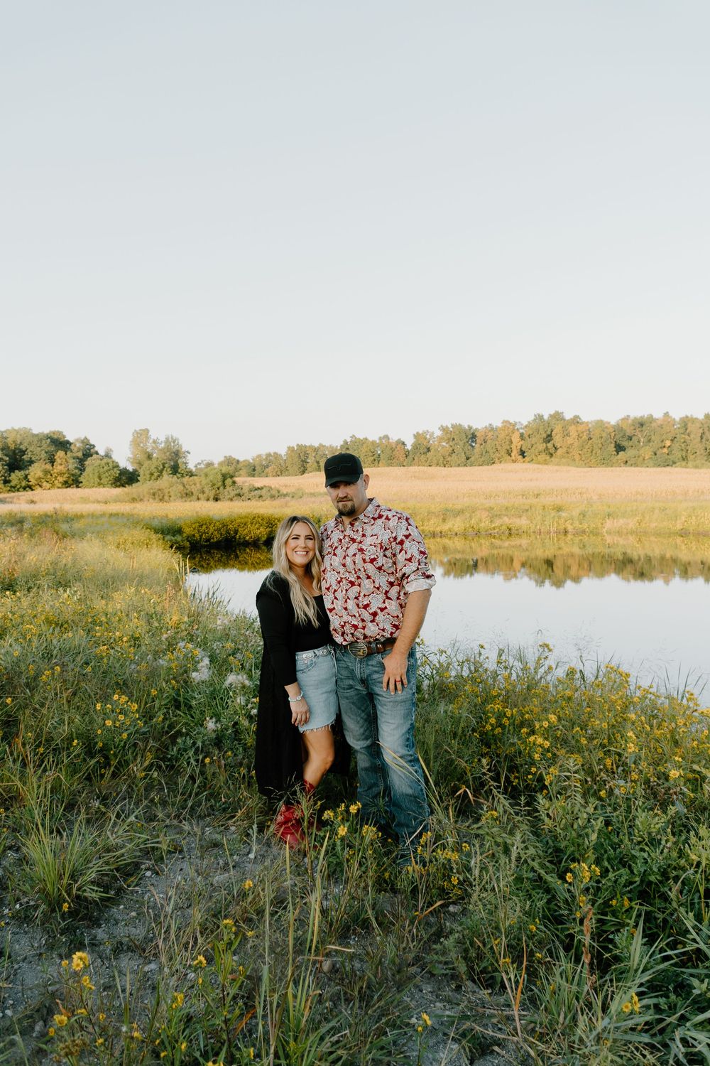 Couple enjoying a romantic moment together by a serene lake surrounded by wildflowers at golden hour.