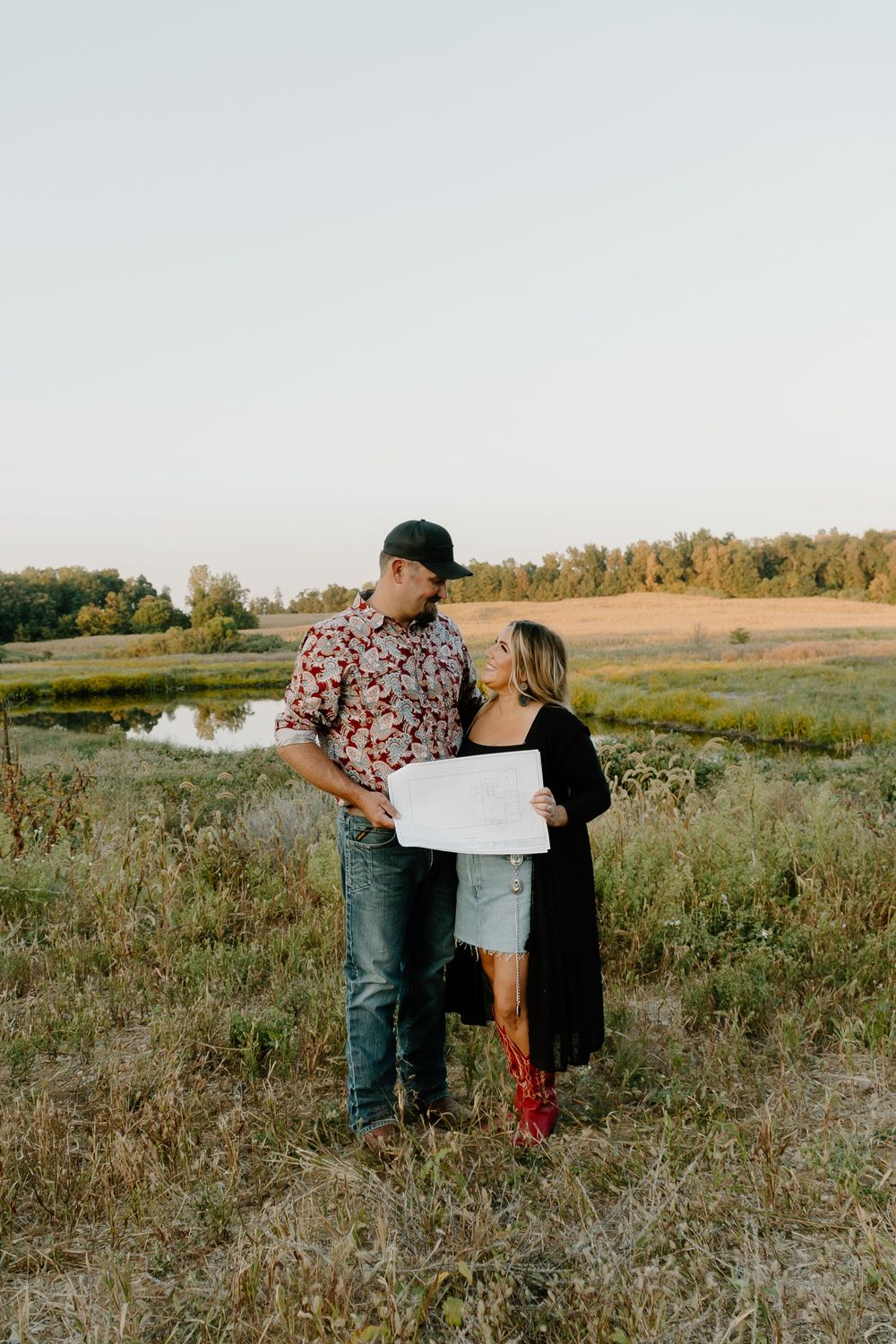 A couple stands together in a golden autumn field looking at a map during sunset.