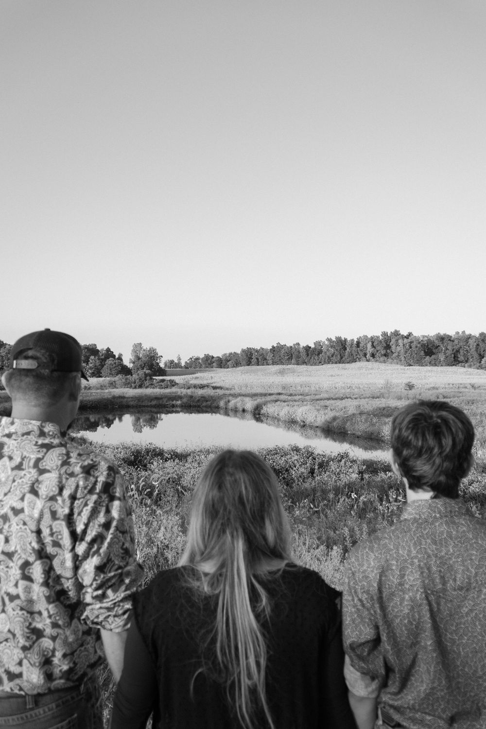 A black and white panoramic series of figures looking out across a rural landscape with trees and fields.
