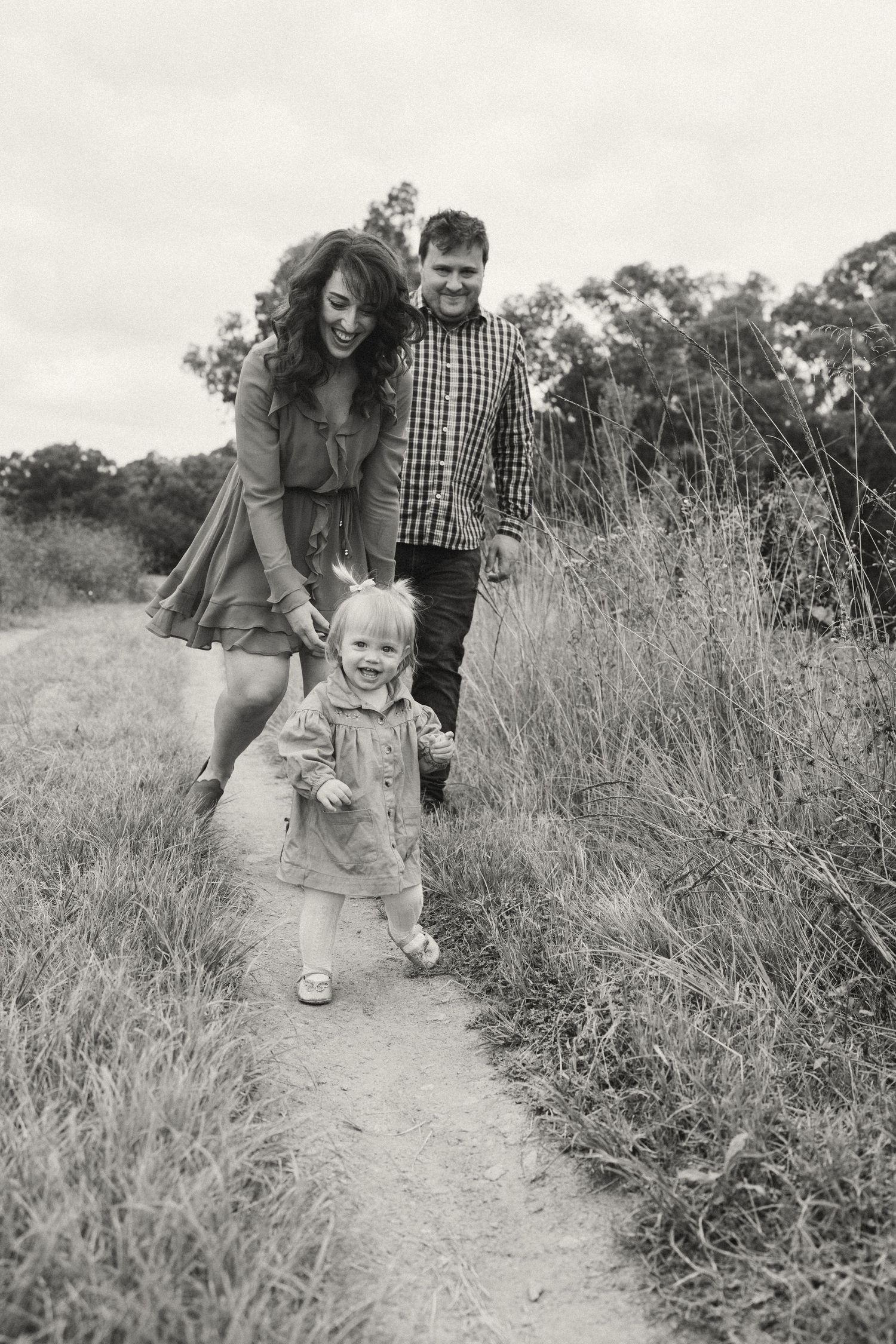 A family walks together on a dirt path through tall grass.
