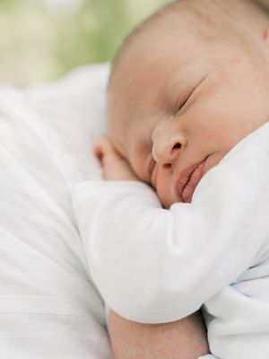 A peaceful sleeping baby swaddled in soft white blankets rests against a light background.