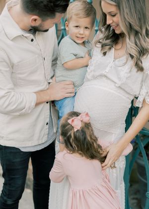 Family wearing white and pink outfits share tender moments together during an outdoor photo session.