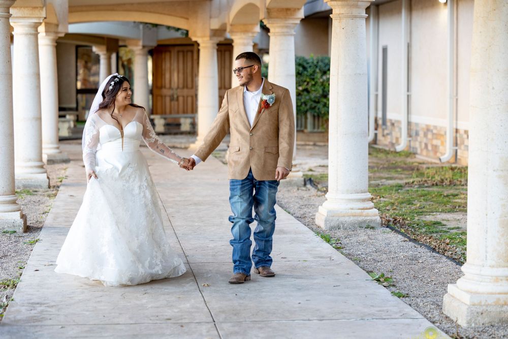 Newlyweds walking hand in hand along a columned walkway in wedding attire.