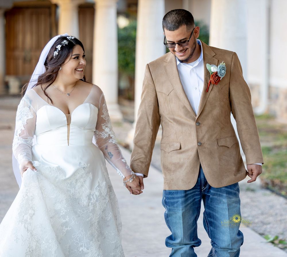 Bride in lace gown and groom in tan blazer walking together outdoors.