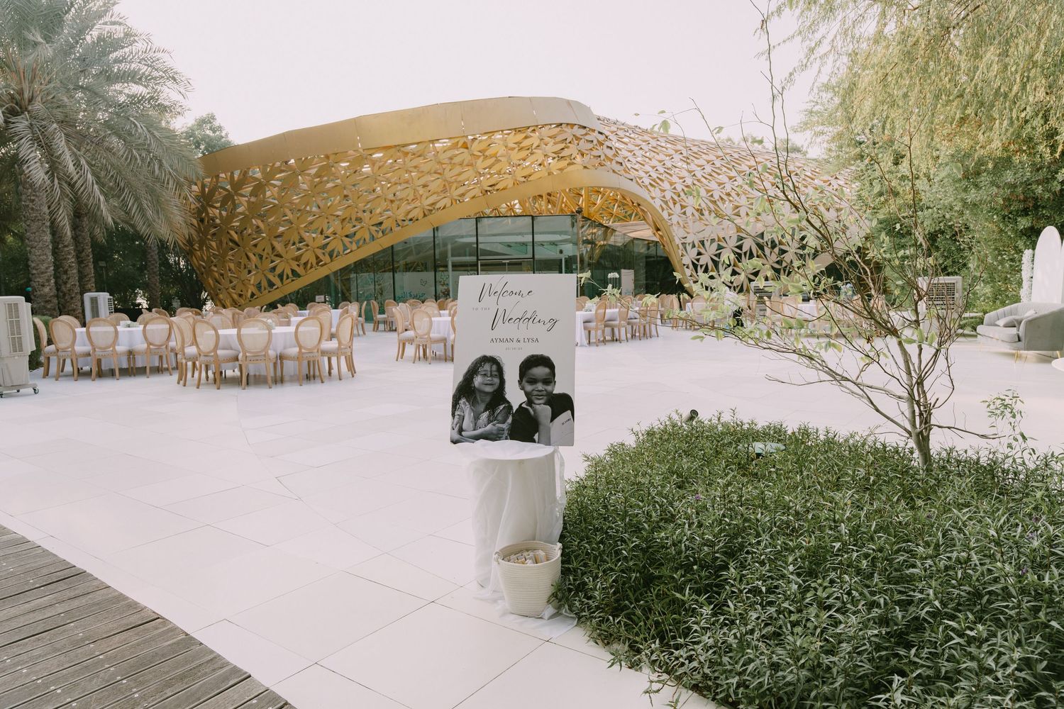 Modern curved architectural structure with outdoor seating and palm trees in an event space setting.