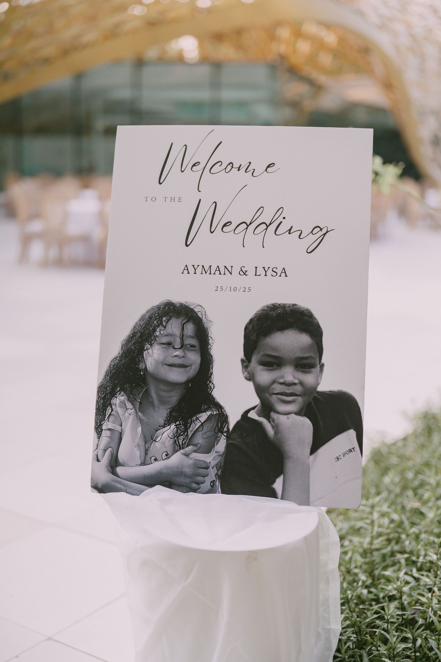 Wedding stationery featuring black and white photos arranged on grass with welcome and wedding text.