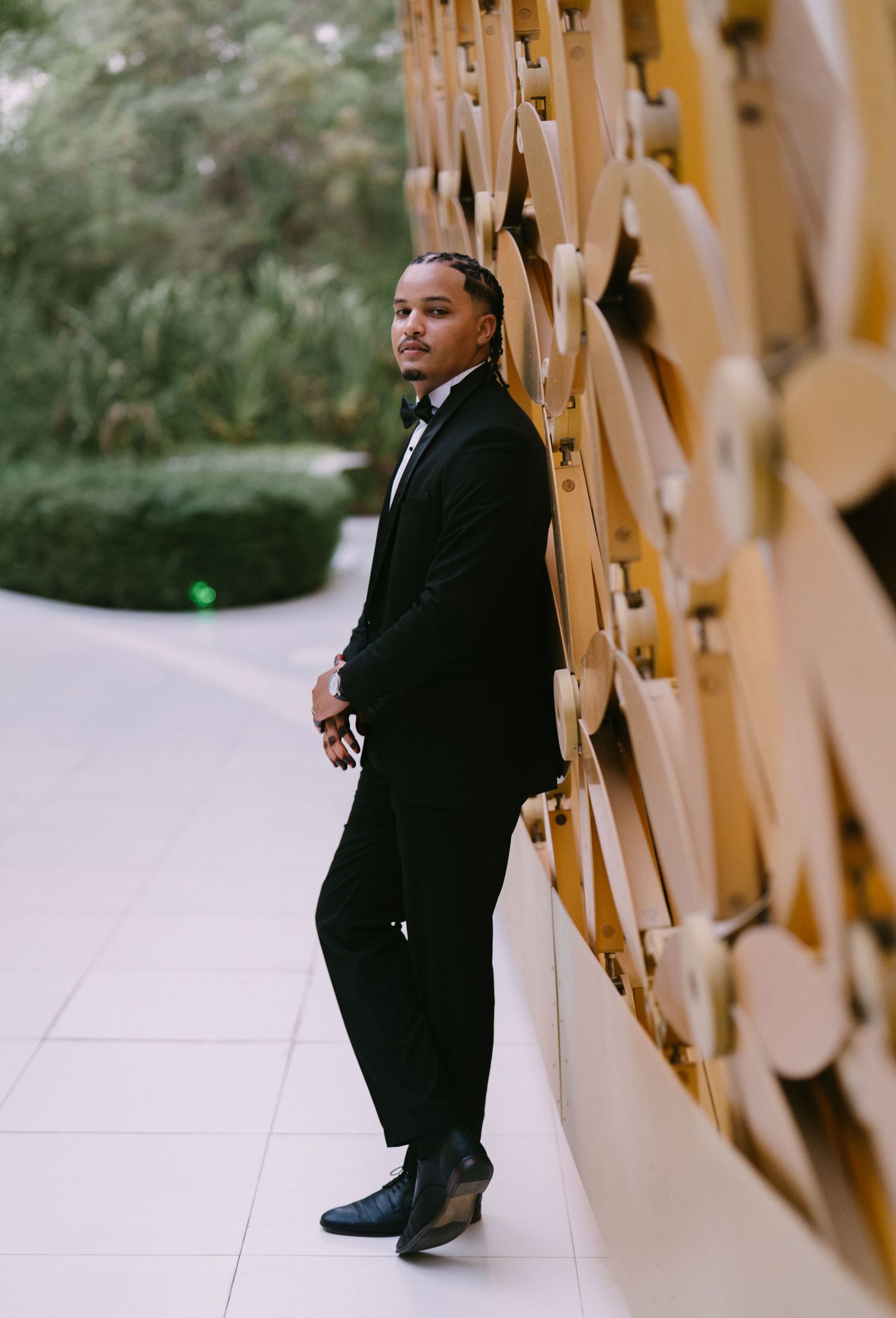 A person wearing a black blazer and boots poses against a beige wall in a stylish fashion photoshoot series.