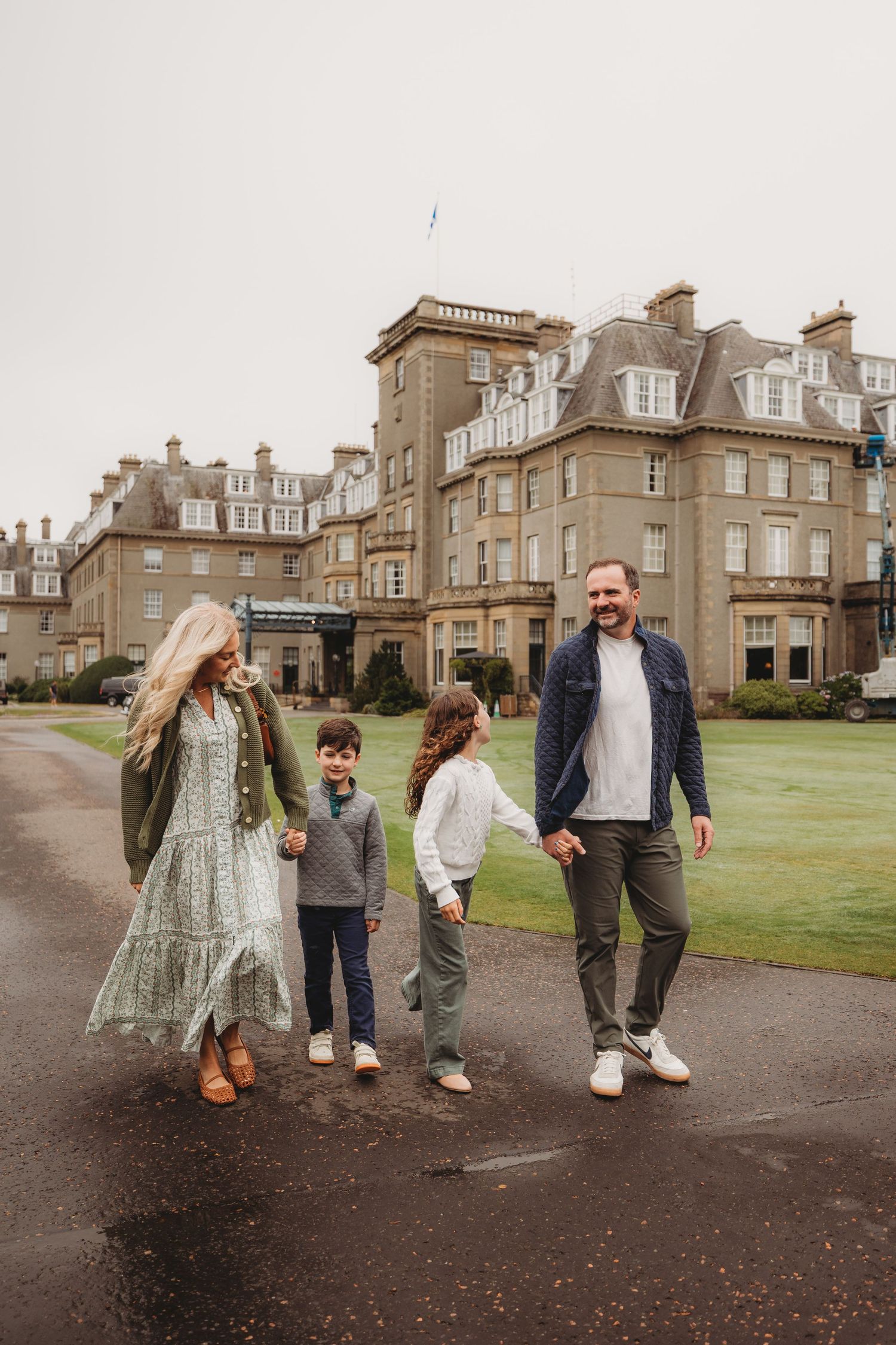 Group walking and laughing together on path outside grand historic stone mansion on overcast day.