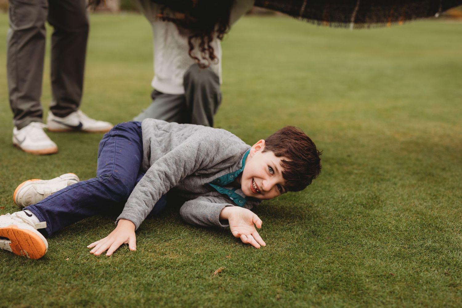 A person lies playfully on lush green grass during a sunny day outdoors.