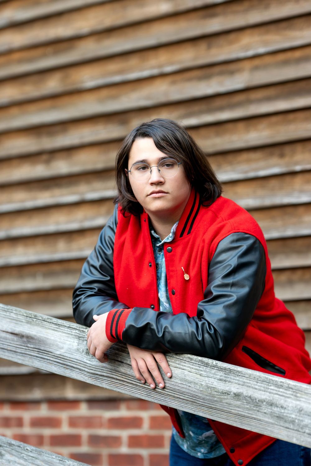 Teen in red varsity jacket leans on wooden railing outdoors.