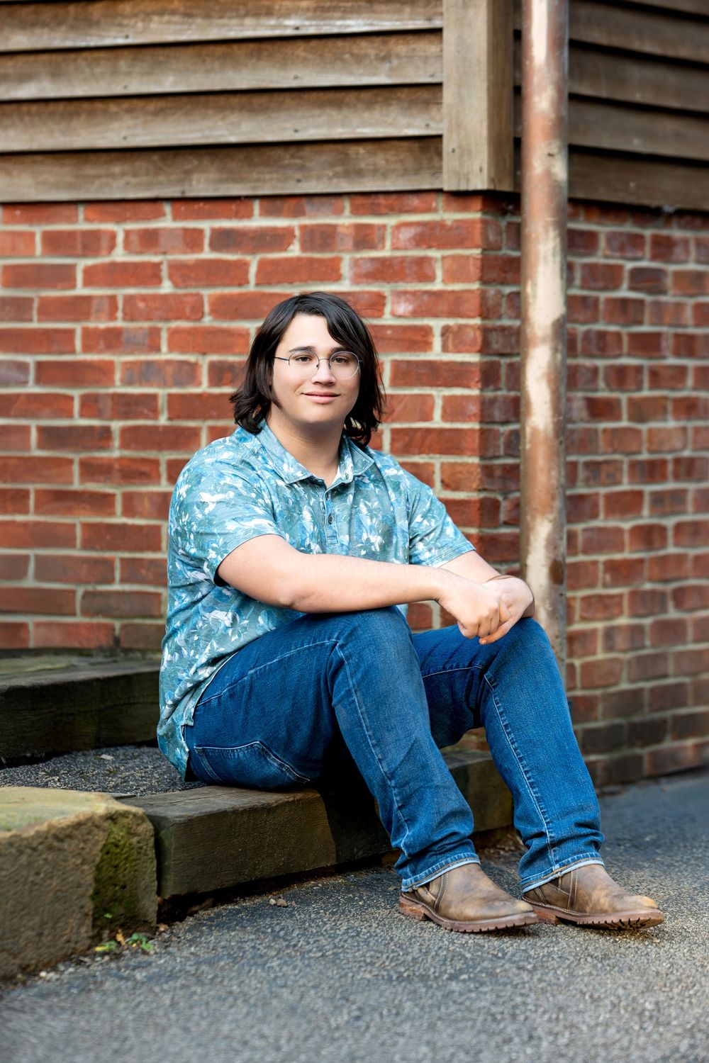 Teen in teal shirt sits on steps against brick wall smiling.