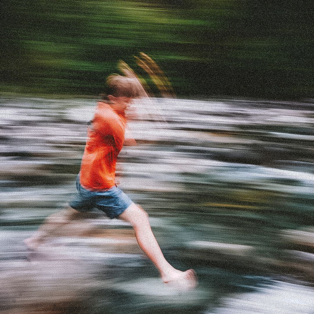 Motion blur sequence of a person in orange jumping across water.