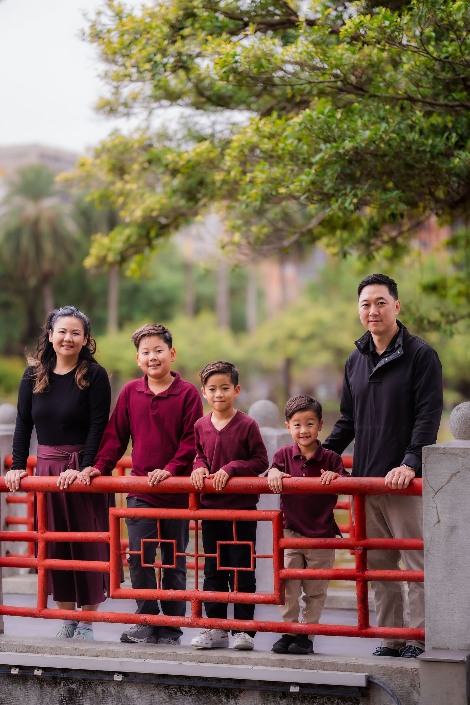 Family group poses together on grassy hill with Taipei 101 tower visible in background on sunny day.